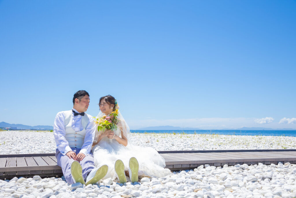 大阪のマーブルビーチでフォトウェディング中の新郎新婦がスニーカー姿で砂浜に座るカジュアルなショット