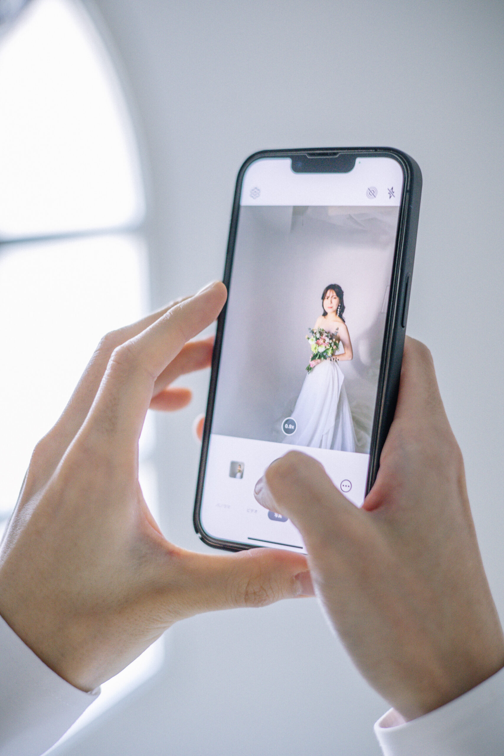 大阪の阿部写真館のスタジオで持ち込みのスマホを使い新婦のウェディングドレス姿を撮影する新郎