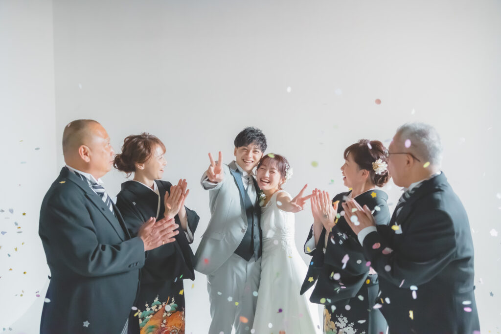 大阪のフォトウェディングで洋装の新郎新婦が和装の両親に見守られながらピースサインをする家族写真