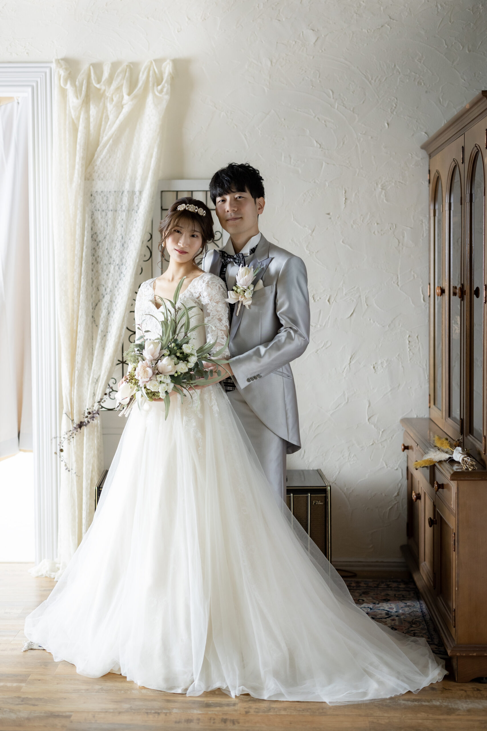 シルバーのタキシードと白いウェディングドレスを着て立つ新郎新婦