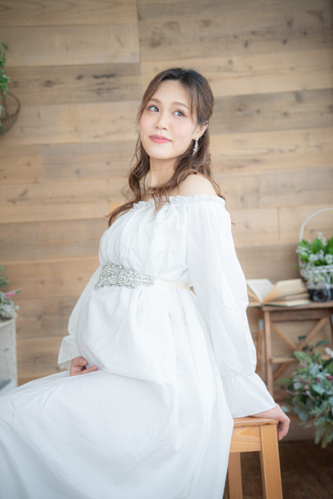 白いふんわりした長袖ドレスで椅子に座るお腹を出さないマタニティフォト