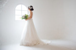 大阪フォトウェディングでAラインのウェディングドレスを着てブーケを持ち窓の外を眺める新婦のソロショット